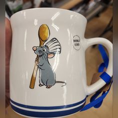 a white mug with a cartoon mouse holding a wooden spoon in it's mouth