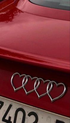 three hearts are attached to the hood of a red sports car with chrome lettering on it