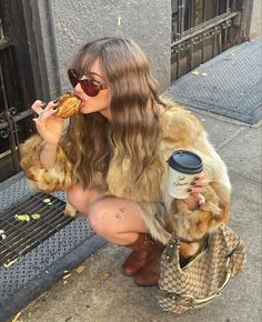 a woman is sitting on the sidewalk eating pizza and drinking from a cup while holding a coffee mug