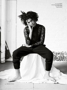 a man with dreadlocks sitting on top of a white sheet