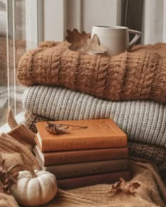 a stack of books sitting on top of a bed next to a cup and pumpkin