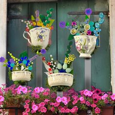 three flower pots with flowers in them on a window sill next to pink and purple flowers