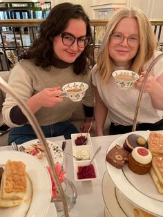 two women sitting at a table with desserts and drinks in front of their faces