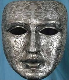 a silver mask with ornate designs on it's face and eyes, in front of a blue background