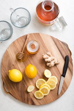 a cutting board with lemons, ginger and honey on it next to some glasses