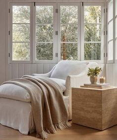 a white bed sitting next to two windows in a room with wooden floors and walls