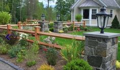 a wooden fence in front of a house surrounded by flowers and plants with a lamp post