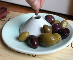 a hand is picking up some olives from a plate