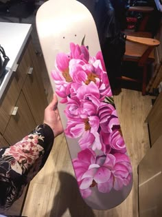 a person holding a skateboard with pink flowers painted on the bottom and side of it