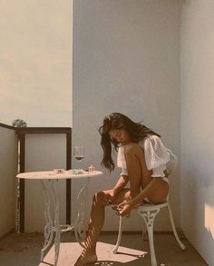 a woman sitting at a table on top of a balcony next to a glass of wine