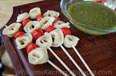 some food is on a wooden tray with toothpicks and sauce in a glass bowl