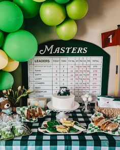 a table topped with lots of food next to green balloons and a sign that says masters