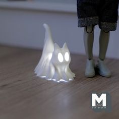 a toy figure standing next to a small white cat on a wooden floor with the light shining through it's eyes