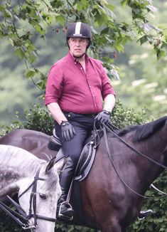 a man riding on the back of a brown horse next to a white and black horse