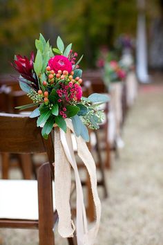 flowers are tied to the back of wooden chairs at an outdoor wedding ceremony in fall