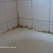 the corner of a bathroom with white tile and water stains on the walls, in need of repair