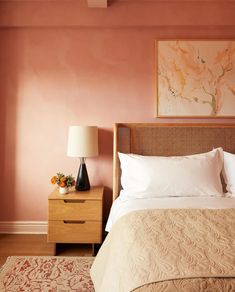 a bed in a bedroom with pink walls and white linens on the headboard