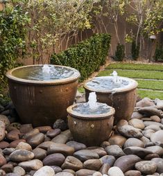 two water fountains sitting on top of a rock covered ground next to a lush green yard