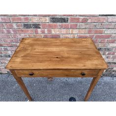 a small wooden table sitting in front of a brick wall with one drawer open and the other closed