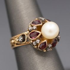 Glowing Rhodolite Garnet Cultured Pearl and Diamond Slice Mid Century Georgian Revival Statement Ring in 14k Yellow Gold Crafted in mid-century with definite nods to Georgian design, this ring features a gorgeous glowing pearl atop bezel set rhodolite garnets separated by tiny diamond slices. The pearl is cultured and measures 7.41mm, with an ivory color and strong reflections. There are six of the rhodolite garnets- red with a pinkish hue. The garnets measure about 5 x 3mm, calculating to 0.15c Georgian Design, Georgian Revival, Pearl Cocktail Ring, Garnet Ring Vintage, Garnet And Diamond Ring, Ruby Rings, Rose Gold Accents, Garnet Jewelry, Celestial Jewelry