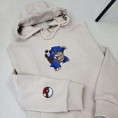 a white sweatshirt with a blue pokemon embroidered on it