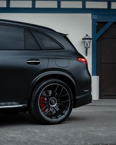 the rear end of a black mercedes suv parked in front of a garage with blue doors