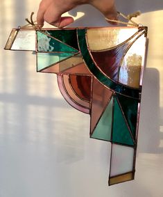 a hand is holding a stained glass suncath in front of a white wall