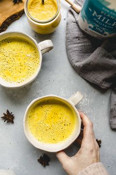 two mugs filled with yellow liquid on top of a table next to cinnamon sticks