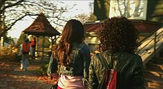 two women walking down the street in front of a house with trees and leaves on it