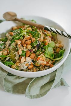 a white bowl filled with rice and vegetables on top of a green napkin next to a wooden spoon