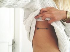 a woman's stomach with a small black arrow tattoo on her left side ribcage