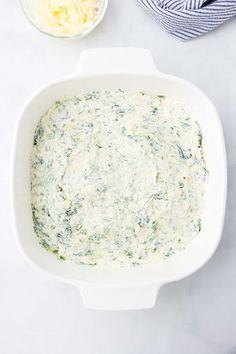 a bowl filled with cheese and spinach on top of a white counter next to a blue towel