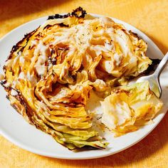 a white plate topped with artichokes covered in sauce and a fork next to it