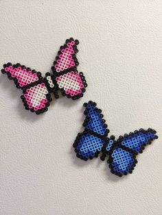 two blue and pink butterfly brooches sitting on top of a white table next to each other