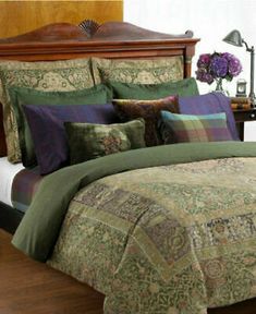 a bed covered in green and purple comforter next to a night stand with flowers on it