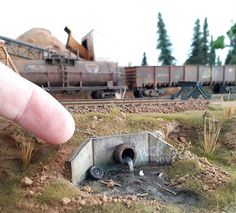 a hand is pointing at a small hole in the ground with a train on it