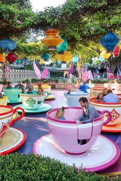 people are sitting in colorful teacups at an amusement park with trees and decorations