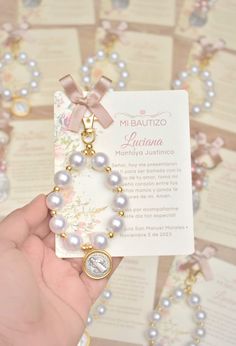 a hand holding a bracelet with pearls and a medal on it's side, in front of some cards