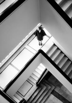 black and white photograph of person standing on top of stairs in an office building, looking up at the ceiling