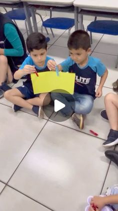 three children sitting on the floor in front of desks and one boy is holding a sign