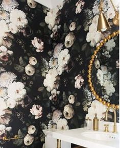 a white sink sitting under a mirror next to a black and white flower wallpaper