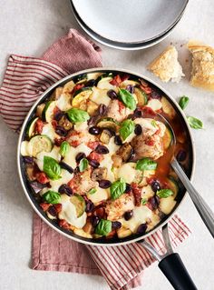 a skillet filled with pasta and vegetables next to a bowl of bread on the side