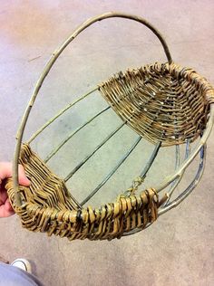 a person holding a basket made out of wicker and metal bars on the ground