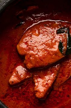 a close up of a meat dish in a pot with red sauce on the side