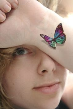 a girl with a butterfly tattoo on her arm covering her eyes and looking at the camera