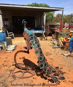 a peacock statue sitting on top of a dirt field next to a building with lots of junk