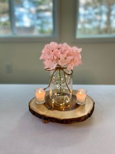 a glass vase filled with pink flowers sitting on top of a wooden slice next to candles