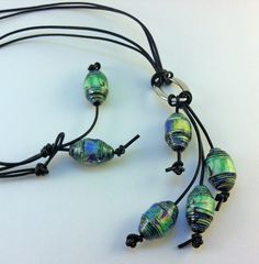 a necklace made with glass beads and black cords on a white surface, next to a pair of earrings