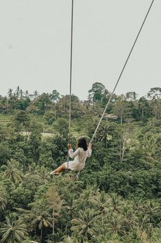 a woman is swinging from a rope in the air with trees and bushes behind her