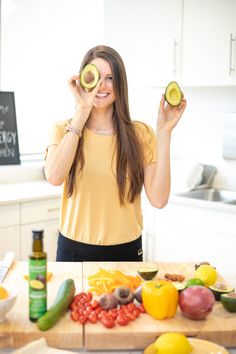 a woman holding an avocado in front of her eyes while standing at a kitchen counter